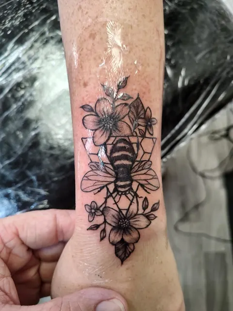 Honey bee surrounded by wildflowers on the inner forearm, black and gray