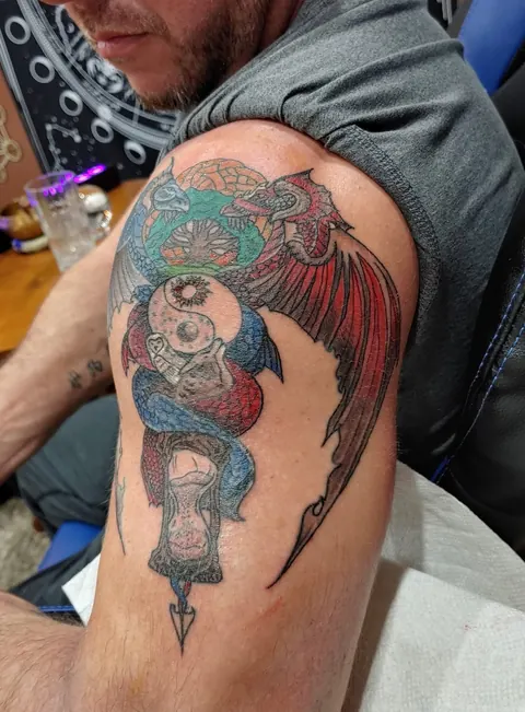 Owl with spread wings gripping a sword through a skull on the upper arm, in color