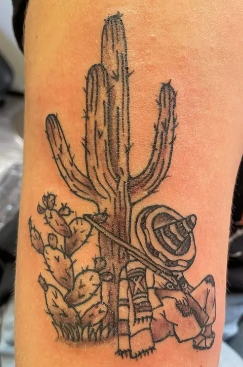 A saguaro cactus with a sleeping cowboy resting against it, black and gray