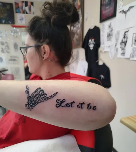 Skeleton hand with the words Let it be in script on the forearm